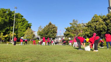 Pati, Endonezya - 08092024: Bir parktaki toplumsal temizlik etkinliğine katılan kırmızı gömlekli bir grup. Güneşli bir günde açık mavi gökyüzü ile birlikte çöp topluyor ve birlikte çalışıyorlar..