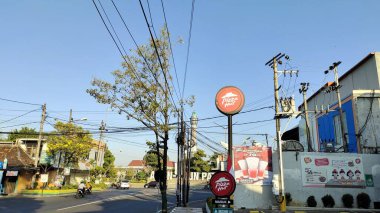 Pati, Endonezya - 08092024: Pizza Hut tabelasının, elektrik hatlarının ve açık mavi gökyüzünün olduğu bir sokak manzarası. Sahne ağaçlar ve binalar içeriyor, canlı bir şehir atmosferi yaratıyor..