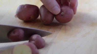 Tahta kesme tahtasındaki bıçakla bebek kırmızı patatesleri dilimlemek.