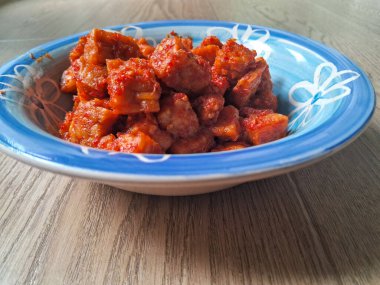 Ahşap arka planda bir kase kırmızı baharatlı orek tempeh.