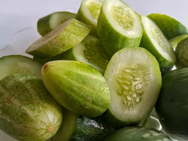 Lalab, beyaz arka planlı şeffaf bir tabakta dilimlenmiş salatalık ve yeşil patlıcan.