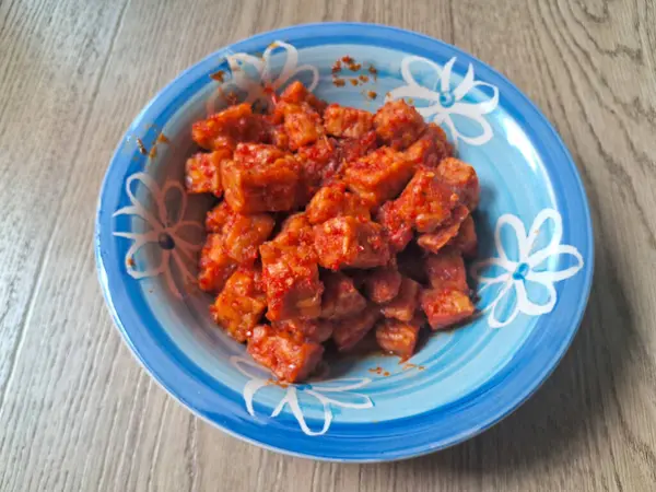 Ahşap arka planda bir kase kırmızı baharatlı orek tempeh.