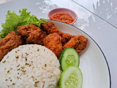 Beyaz bir tabakta salatalık ve salatalık ile servis edilen pirinç ve karage tavuğu. Kırmızı biber soslu, izole edilmiş beyaz bir arka planda.