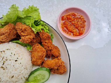 Beyaz bir tabakta salatalık ve salatalık ile servis edilen pirinç ve karage tavuğu. Kırmızı biber soslu, izole edilmiş beyaz bir arka planda.