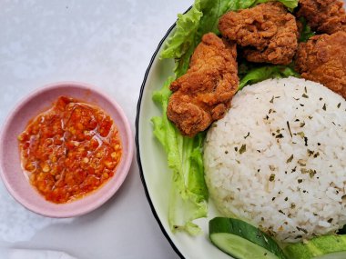 Beyaz bir tabakta salatalık ve salatalık ile servis edilen pirinç ve karage tavuğu. Kırmızı biber soslu, izole edilmiş beyaz bir arka planda.