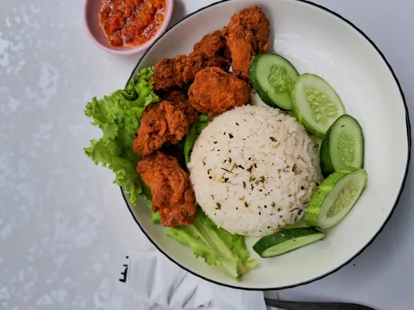 Beyaz bir tabakta salatalık ve salatalık ile servis edilen pirinç ve karage tavuğu. Kırmızı biber soslu, izole edilmiş beyaz bir arka planda.
