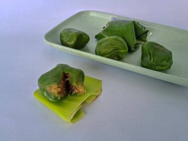 Bugis keki, geleneksel Endonezya aperatifi yumuşak yeşil yapışkan pirinç un keki, tatlı rendelenmiş hindistan cevizi ile doldurulmuş, muz yapraklarına sarılmış, ahşap bir tabakta, beyaz bir arka planda izole edilmiş