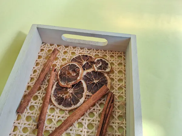 Kurumuş narenciye dilimleri ve tarçın çubukları dokunmuş ahşap tepside, yumuşak pastel arka planda sıcak, kırsal görünüm için ayarlanmış..