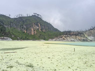 Sülfür gölünün büyüleyici manzarası ve Bandung, Kawah Putih 'deki ahşap yürüyüş yolu. Bu volkanik krater gölü, engebeli tepeler ve uçurumlarla çevrili, eşsiz ve başka dünyalara ait bir manzara yaratır..