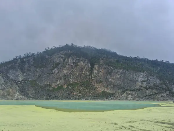 Sülfür gölünün büyüleyici manzarası ve Bandung, Kawah Putih 'deki ahşap yürüyüş yolu. Bu volkanik krater gölü, engebeli tepeler ve uçurumlarla çevrili, eşsiz ve başka dünyalara ait bir manzara yaratır..