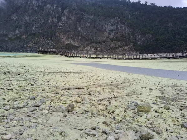 Sülfür gölünün büyüleyici manzarası ve Bandung, Kawah Putih 'deki ahşap yürüyüş yolu. Bu volkanik krater gölü, engebeli tepeler ve uçurumlarla çevrili, eşsiz ve başka dünyalara ait bir manzara yaratır..