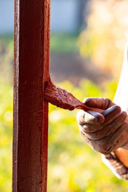 Bir adam köy evindeki ahşap bir pencereyi onarıp boyuyor..