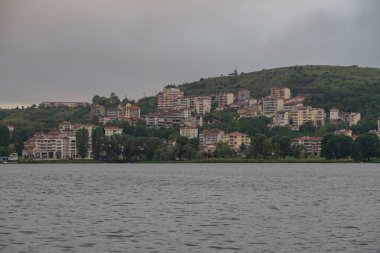 Arka planda dağlarda gölü olan güzel bir manzara. Baharda Yunan kenti Kastoria 'nın manzarası. Dağ gölünün kıyısındaki eski bir kasaba.