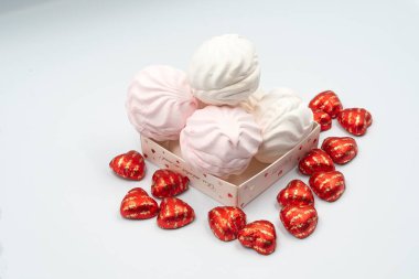 İçinde kalp şeklinde lezzetli çikolatalar ve Sevgililer Günü için beyaz arka planda beyaz pembe şekerlemeler olan bir kutu.