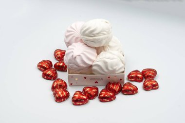 İçinde kalp şeklinde lezzetli çikolatalar ve Sevgililer Günü için beyaz arka planda beyaz pembe şekerlemeler olan bir kutu.