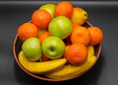 Gri arka planda bir kasede taze olgun meyveler. Meyve karışımı mandalina, armut, muz, elma. Sağlıklı beslenme. Vitaminler.