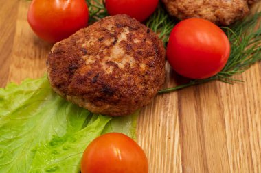 Ahşap arka planda sebzeli kızarmış tavuk pirzolası. Tahtada domatesli et topları ve otlar..