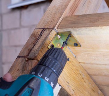 Bir adam matkapla çalışır. Usta elektrikli matkap kullanarak ahşap bir bank kuruyor..