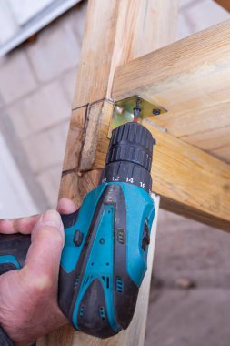 Bir adam matkapla çalışır. Usta elektrikli matkap kullanarak ahşap bir bank kuruyor..