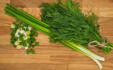 Taze yeşil soğanlar ve ahşap kesme tahtasındaki dereotlar.