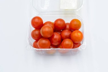 Beyaz arka planda plastik bir kabın içinde taze kiraz domatesleri.