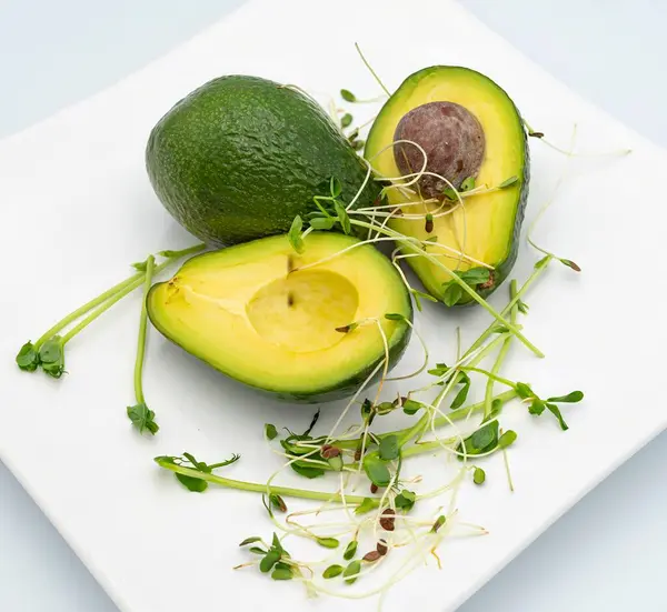 Beyaz bir tabakta taze avokado dilimleri ve mikro yeşiller. Avokado yarıları. Sağlıklı yemek..