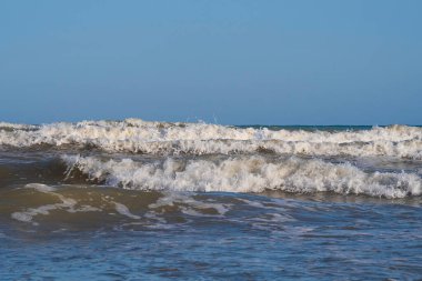 Denizde hafif bir fırtına. Beyaz köpüklü ve beyaz kapaklı dalgalar kumlu bir plajın kıyısında yuvarlanıyor. İspanya 'da tatil köyü. Deniz kıyısının güzel manzarası