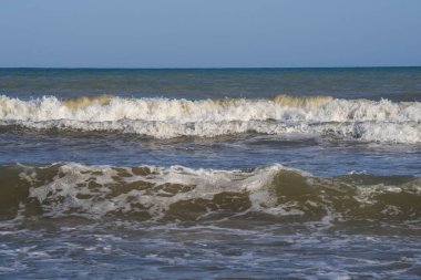 Denizde hafif bir fırtına. Beyaz köpüklü ve beyaz kapaklı dalgalar kumlu bir plajın kıyısında yuvarlanıyor. İspanya 'da tatil köyü. Deniz kıyısının güzel manzarası