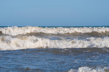 Denizde hafif bir fırtına. Beyaz köpüklü ve beyaz kapaklı dalgalar kumlu bir plajın kıyısında yuvarlanıyor. İspanya 'da tatil köyü. Deniz kıyısının güzel manzarası