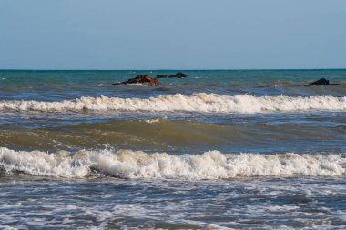 Denizde hafif bir fırtına. Beyaz köpüklü ve beyaz kapaklı dalgalar kumlu bir plajın kıyısında yuvarlanıyor. İspanya 'da tatil köyü. Deniz kıyısının güzel manzarası