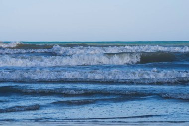 Denizde hafif bir fırtına. Beyaz köpüklü ve beyaz kapaklı dalgalar kumlu bir plajın kıyısında yuvarlanıyor. İspanya 'da tatil köyü. Deniz kıyısının güzel manzarası