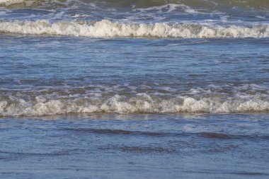 Denizde hafif bir fırtına. Beyaz köpüklü ve beyaz kapaklı dalgalar kumlu bir plajın kıyısında yuvarlanıyor. İspanya 'da tatil köyü. Deniz kıyısının güzel manzarası