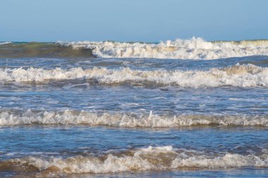 Denizde hafif bir fırtına. Beyaz köpüklü ve beyaz kapaklı dalgalar kumlu bir plajın kıyısında yuvarlanıyor. İspanya 'da tatil köyü. Deniz kıyısının güzel manzarası