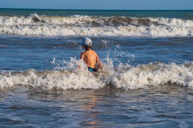 Yazın denizin dalgalarında oynayan küçük bir çocuk. Aktif tatil ve aktif yaşam kavramı.