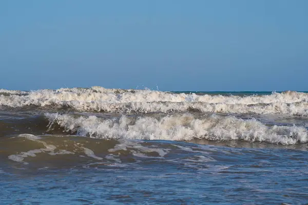 Denizde hafif bir fırtına. Beyaz köpüklü ve beyaz kapaklı dalgalar kumlu bir plajın kıyısında yuvarlanıyor. İspanya 'da tatil köyü. Deniz kıyısının güzel manzarası