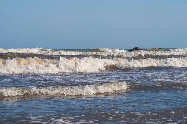 Denizde hafif bir fırtına. Beyaz köpüklü ve beyaz kapaklı dalgalar kumlu bir plajın kıyısında yuvarlanıyor. İspanya 'da tatil köyü. Deniz kıyısının güzel manzarası