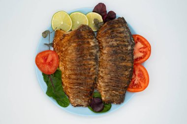 Sebzeli ızgara balık ve beyaz arka planda yeşillikler.