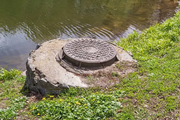 Şehir parkındaki bir göletin kıyısında rögar kapağı.