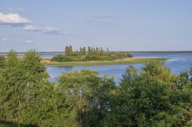 Geniş bir nehir ve kıyı boyunca yoğun bitki örtüsüyle güzel bir manzara..
