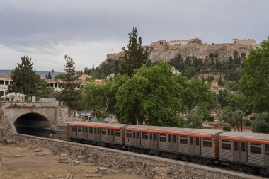 Yunanistan 'ın Monastyraki bölgesindeki Atina' daki antik Akropolis kentinden bir metro treni geçiyor. Atina, 23 Mayıs 2025