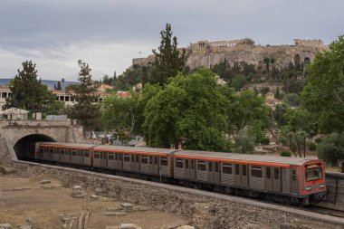 Yunanistan 'ın Monastyraki bölgesindeki Atina' daki antik Akropolis kentinden bir metro treni geçiyor. Atina, 23 Mayıs 2025