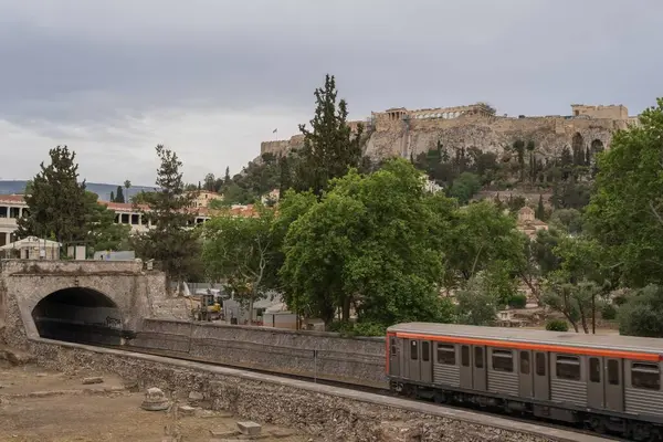 Yunanistan 'ın Monastyraki bölgesindeki Atina' daki antik Akropolis kentinden bir metro treni geçiyor. Atina, 23 Mayıs 2025