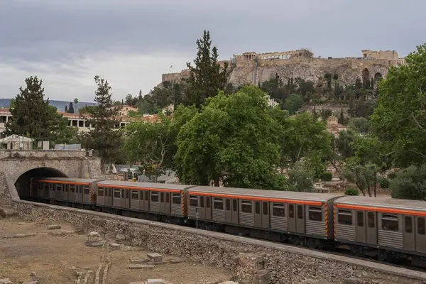 Yunanistan 'ın Monastyraki bölgesindeki Atina' daki antik Akropolis kentinden bir metro treni geçiyor. Atina, 23 Mayıs 2025