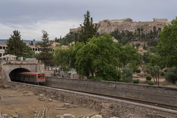 Yunanistan 'ın Monastyraki bölgesindeki Atina' daki antik Akropolis kentinden bir metro treni geçiyor. Atina, 23 Mayıs 2025