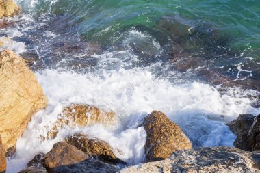 Deniz dalgaları kayalık kıyıya yuvarlanır ve büyük kayalara çarpar, köpük oluşturur..