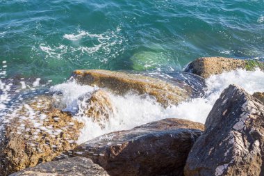 Deniz dalgaları kayalık kıyıya yuvarlanır ve büyük kayalara çarpar, köpük oluşturur..