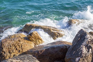 Deniz dalgaları kayalık kıyıya yuvarlanır ve büyük kayalara çarpar, köpük oluşturur..