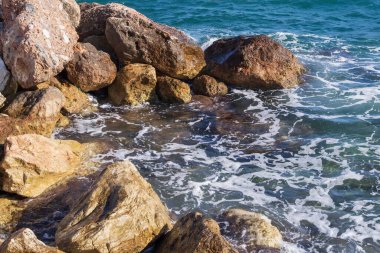 Dalgalar halinde akan turkuaz deniz suyuyla kayalık kıyılar ve kalın beyaz deniz köpüğü oluşturur..
