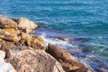 Dalgalar halinde akan turkuaz deniz suyuyla kayalık kıyılar ve kalın beyaz deniz köpüğü oluşturur..