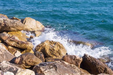 Deniz dalgaları kayalık kıyıya yuvarlanır ve büyük kayalara çarpar, köpük oluşturur..